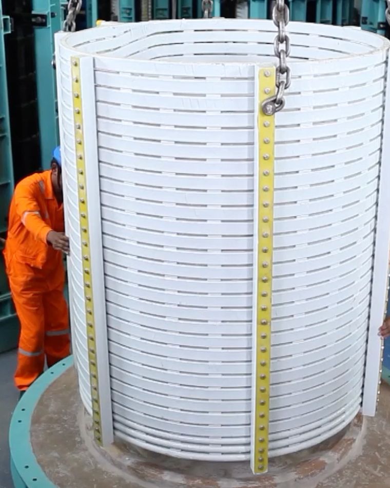 Finished induction furnace coil lifted by crane, two technicians guiding it